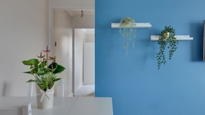 A room with a white table and chairs, a potted plant, and two hanging planters against a blue wall. - BookedUK - Bright flat in Harlow (Harlow)