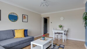 A living room with a grey sofa, a white coffee table, and a dining table with chairs. There is a mirror on the wall and a clock. - BookedUK - Bright flat in Harlow (Harlow)