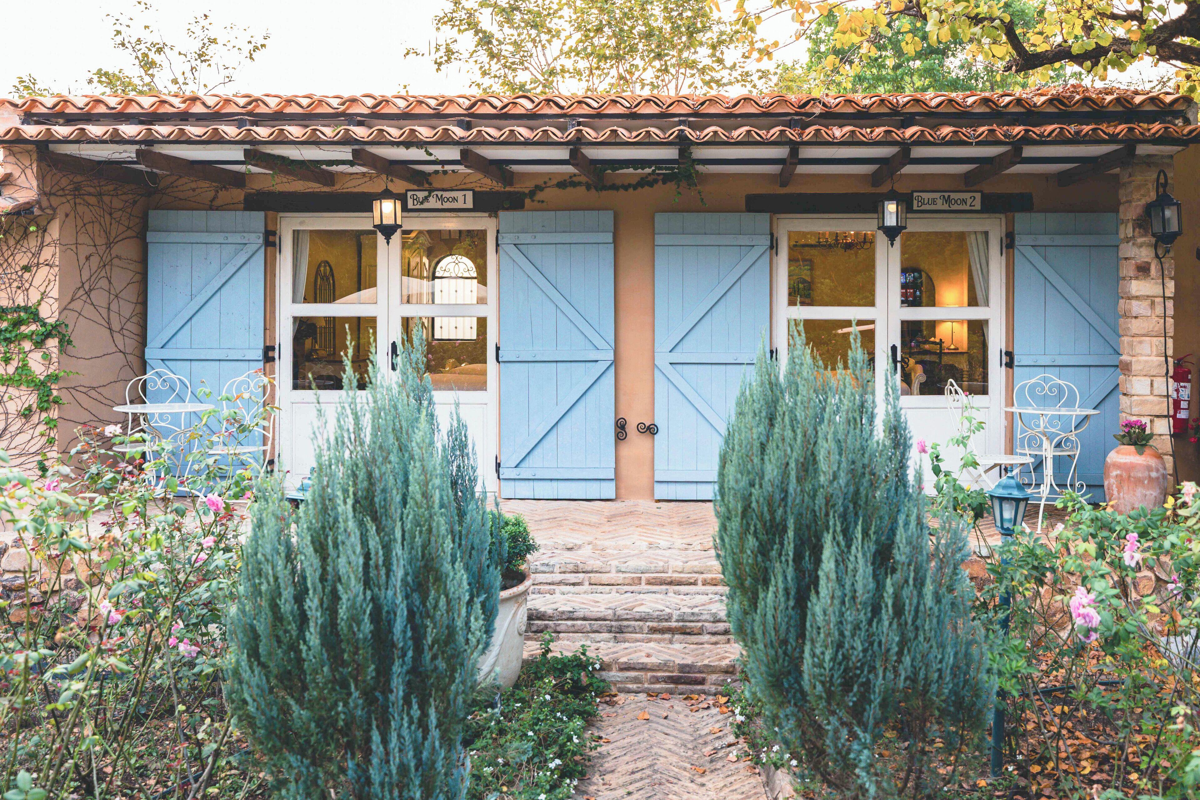 A building with two blue doors labeled 'Blue Moon 1' and 'Blue Moon 2,' a stone staircase, and a garden with potted plants.
