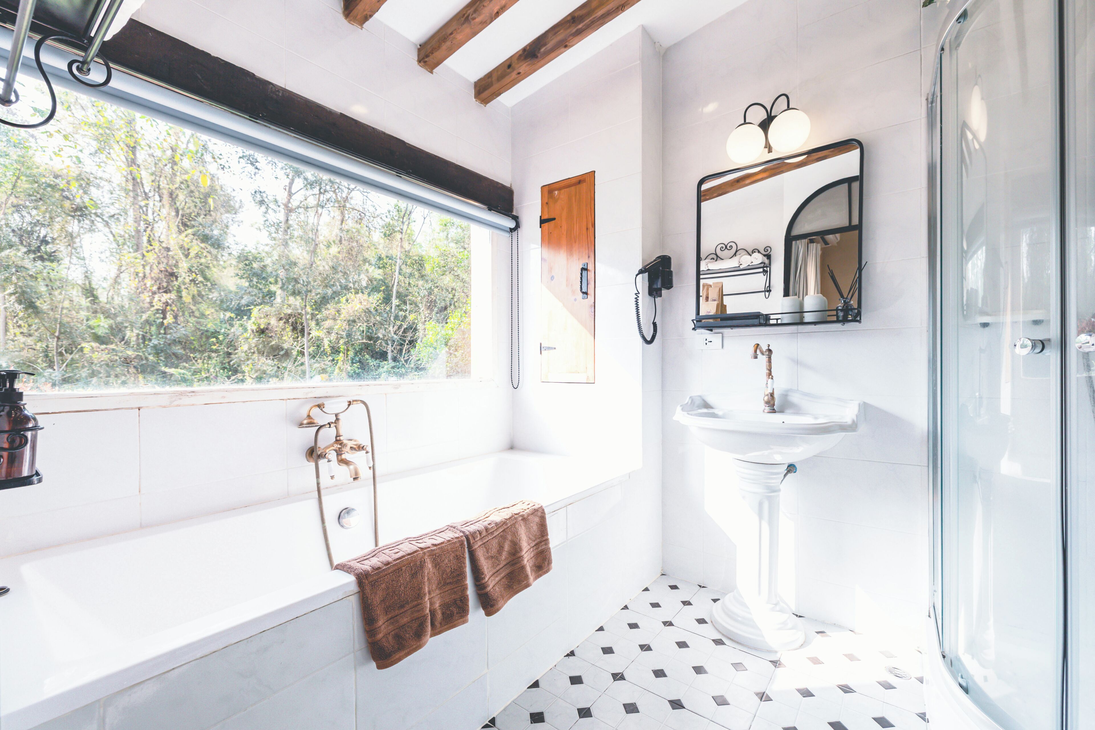 A bathroom with a bathtub, a sink, a glass shower enclosure, and a window with a view of trees.