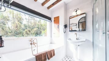 A bathroom with a bathtub, a sink, a glass shower enclosure, and a window with a view of trees.