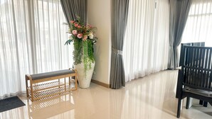 Una habitación amplia con un ventanal grande, un banco de madera, una silla negra y una planta en maceta con flores.