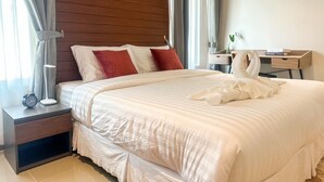 Una cama bien hecha con ropa de cama blanca, un cabecero de madera y una mesita de noche con una lámpara y un despertador.