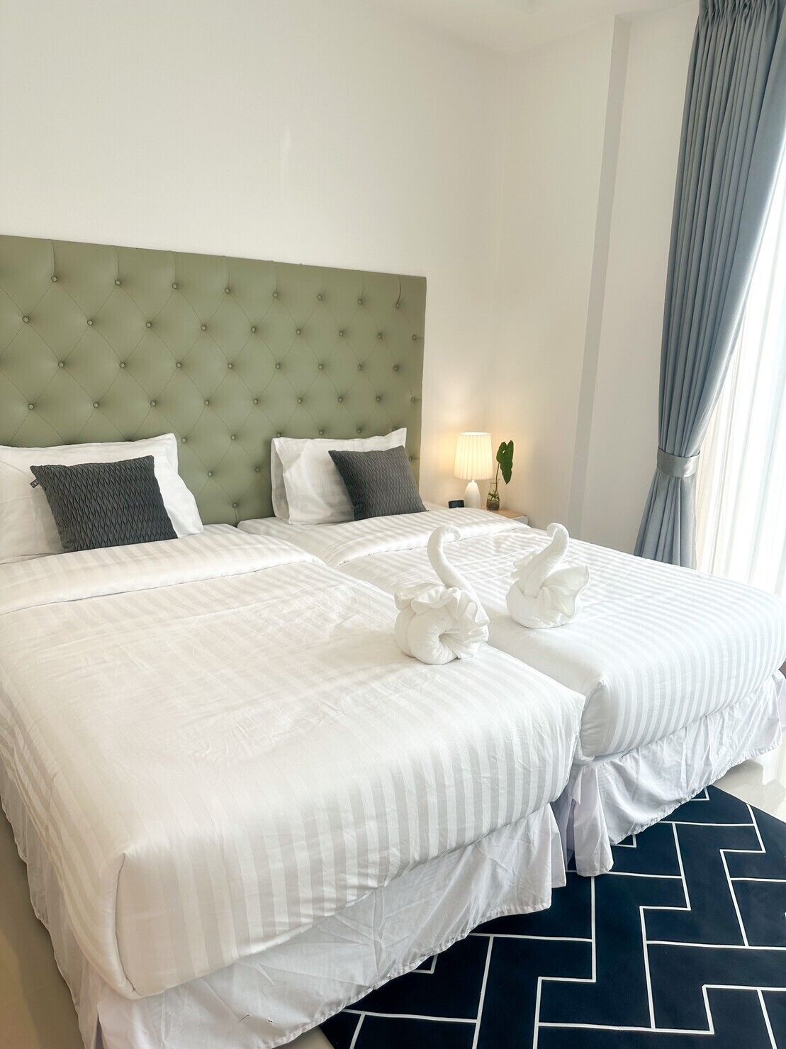 A hotel room with two beds, a green tufted headboard, white bedding, and a black and white patterned floor.