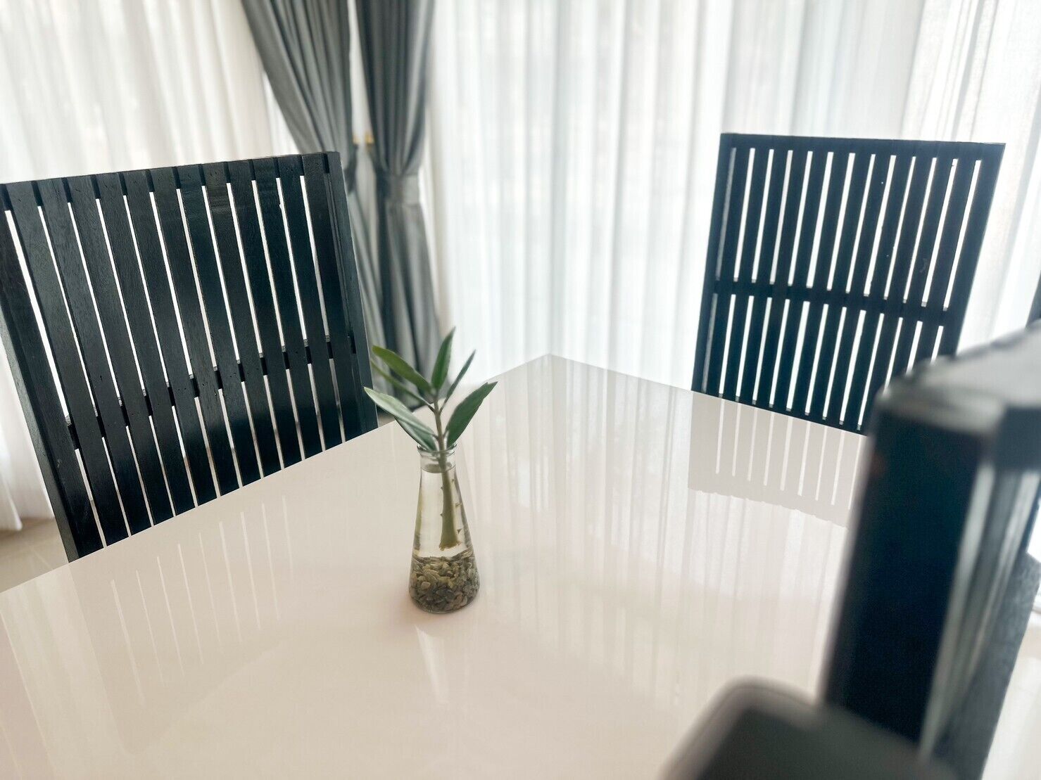 A round table with a glass vase containing a plant, surrounded by black chairs.