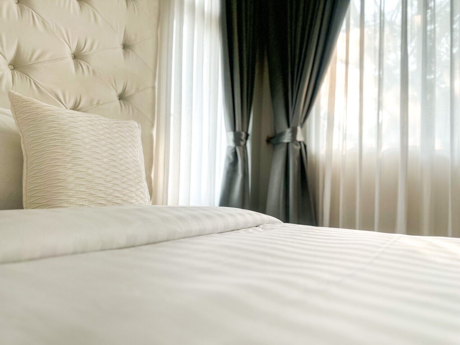 Una cama bien hecha con un cabecero capitonado y una única almohada decorativa.
