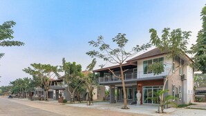 Un edificio residencial moderno de dos pisos con un balcón, rodeado de árboles y un camino pavimentado.