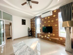 A modern living room with a flat-screen TV, a ceiling fan, and a brick-patterned wall.