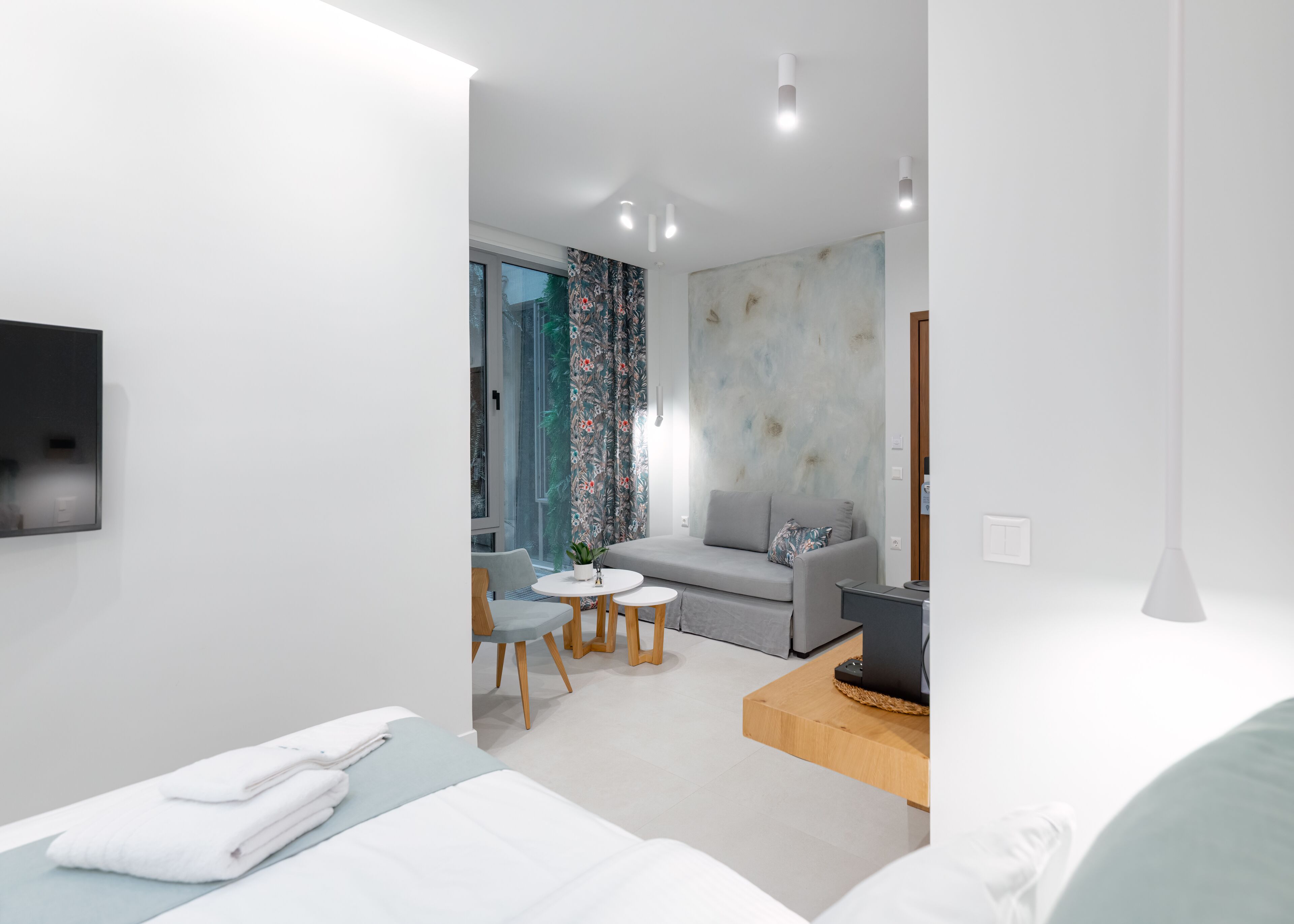 Ein modernes Hotelzimmer mit einem Bett, einem Sofa, einem kleinen Tisch und einem an der Wand befestigten Fernseher.