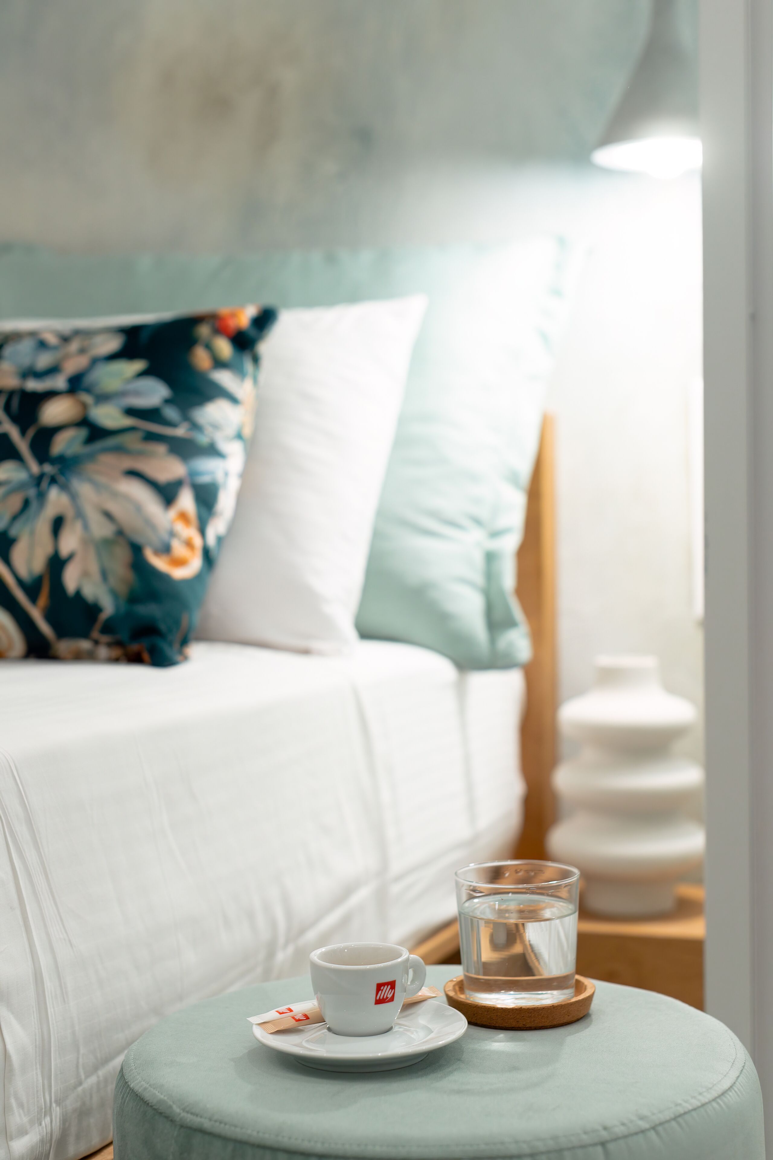 A neatly made bed with a floral pillow, a white pillow, and a bedside table with a glass of water and a cup.