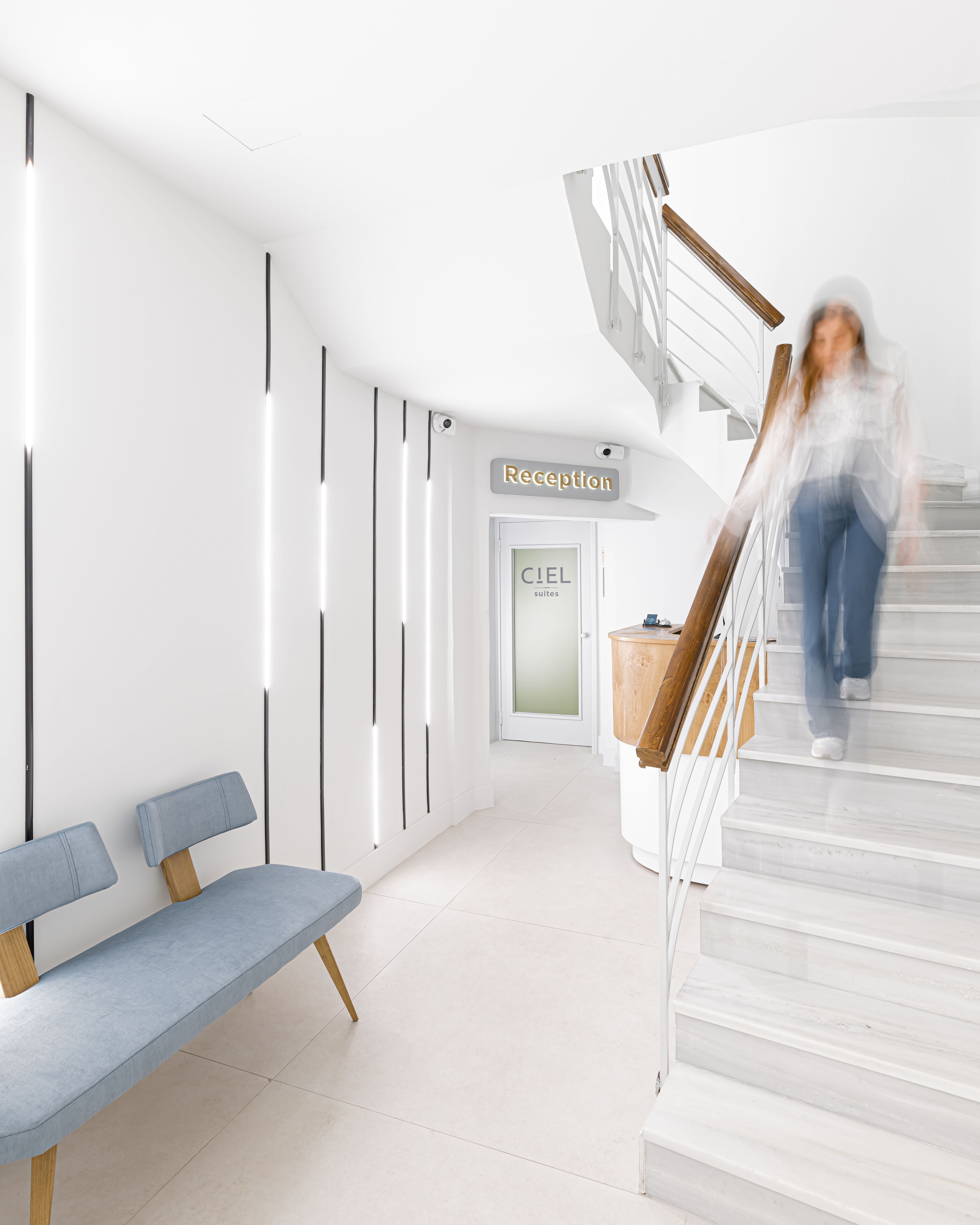 A modern hotel lobby with a reception desk, a staircase, and a bench.