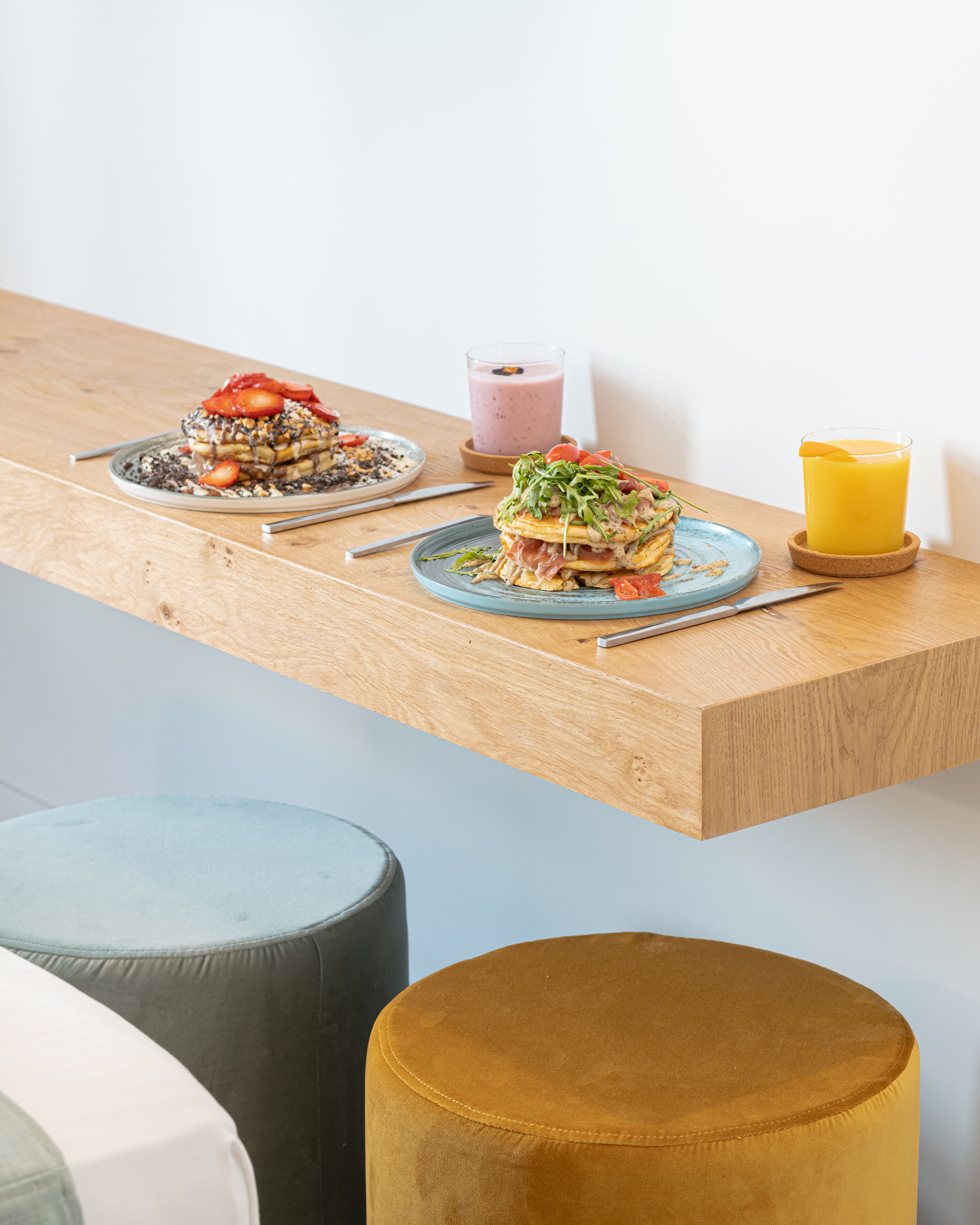 A breakfast setup on a wooden table with two plates of food, a glass of smoothie, and a glass of orange juice.