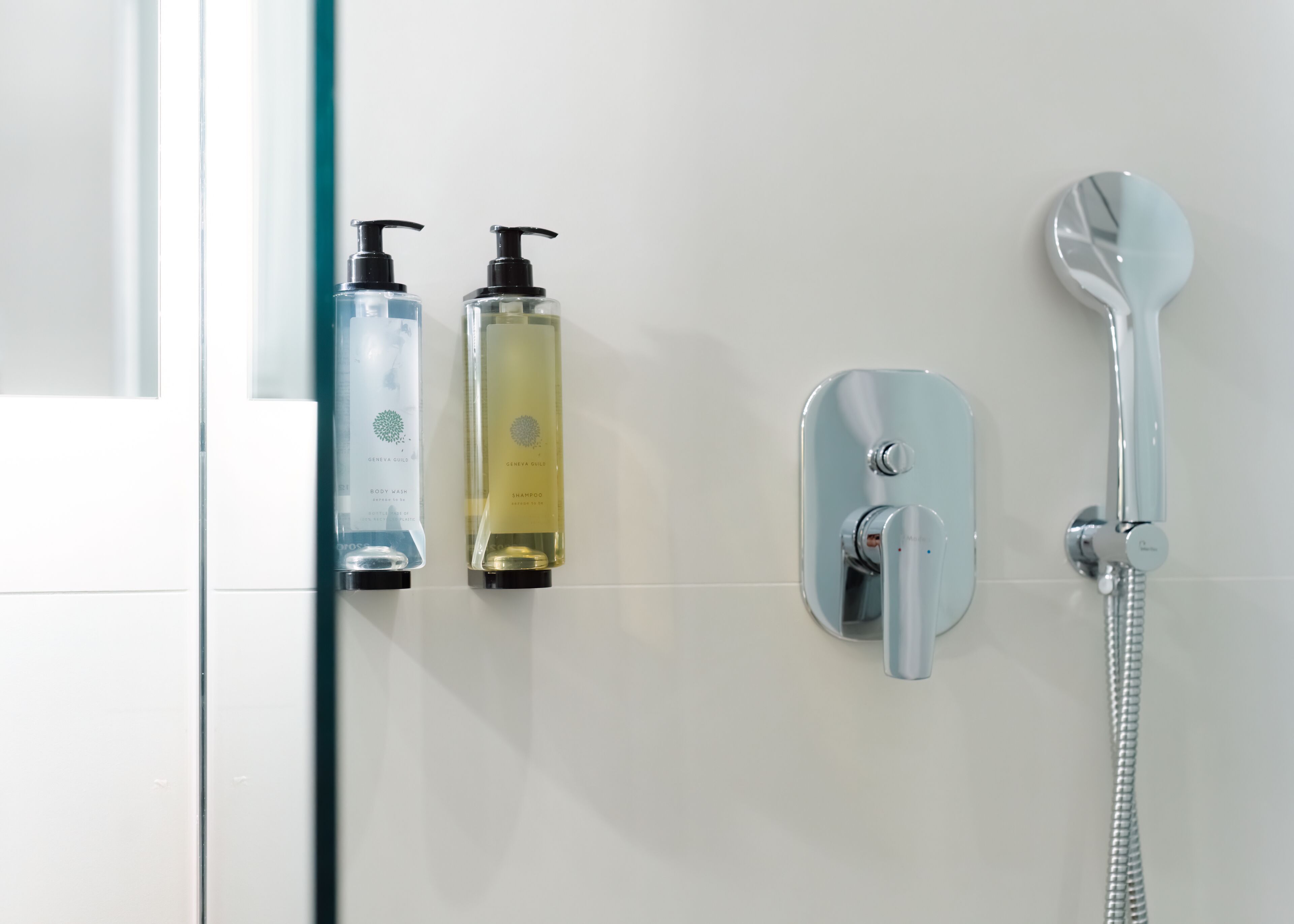 A bathroom with a shower, a hand dryer, and two bottles of body wash and shampoo.