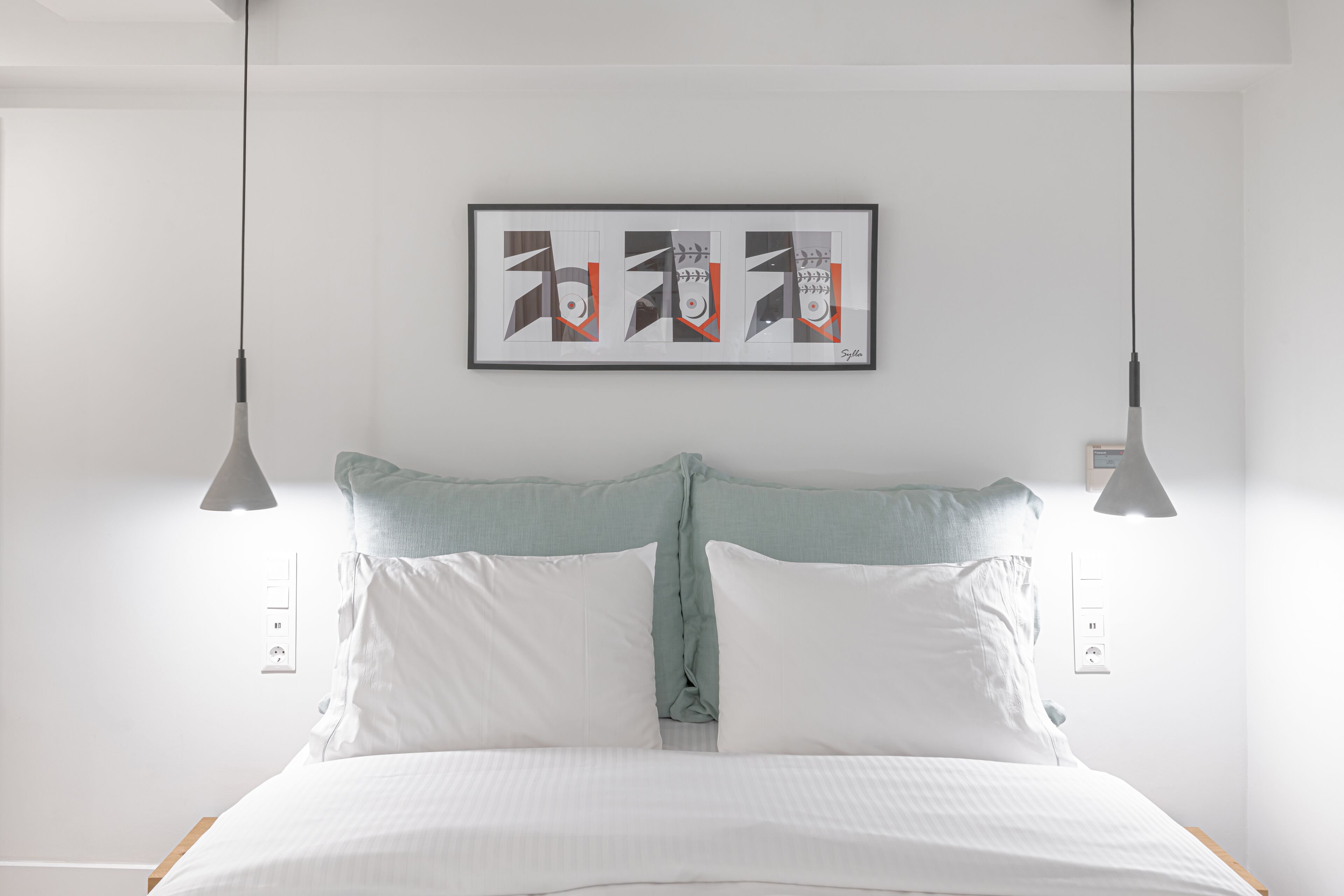 A bedroom with a bed, two bedside lamps, a framed artwork on the wall, and a power outlet.
