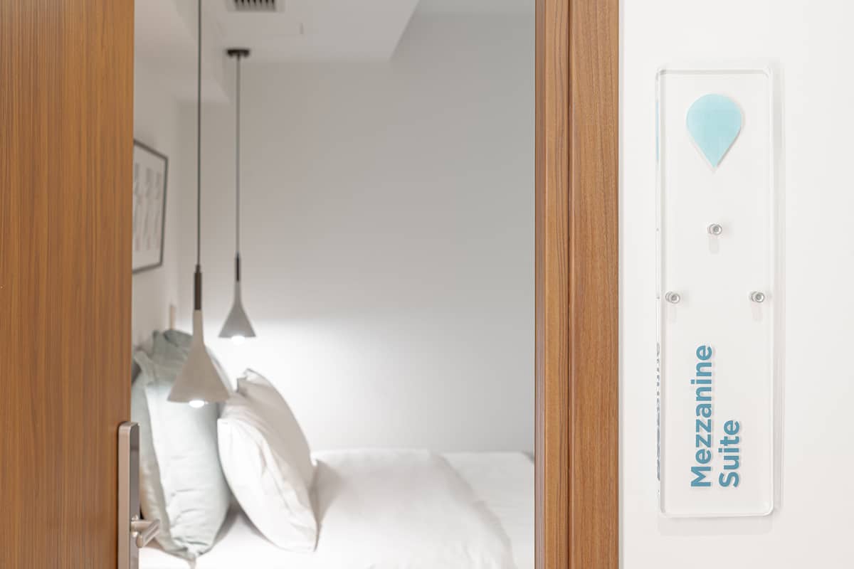 Quarto de hotel com cama, almofadas, luminária pendente e placa indicando que é uma Suíte Mezzanine.