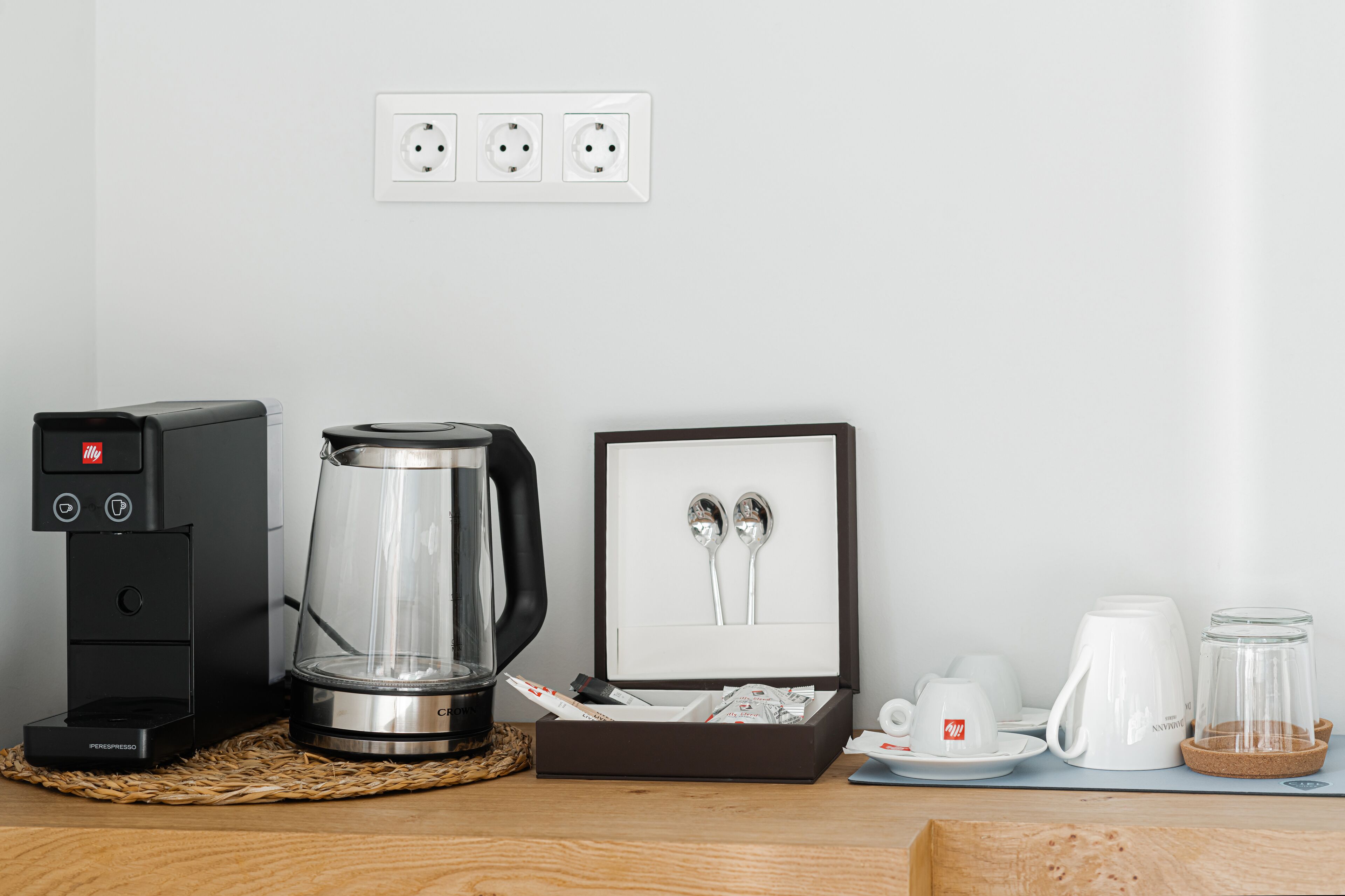 A coffee maker, a glass carafe, a framed spoon set, and a coffee station with cups and a glass jar on a wooden table.