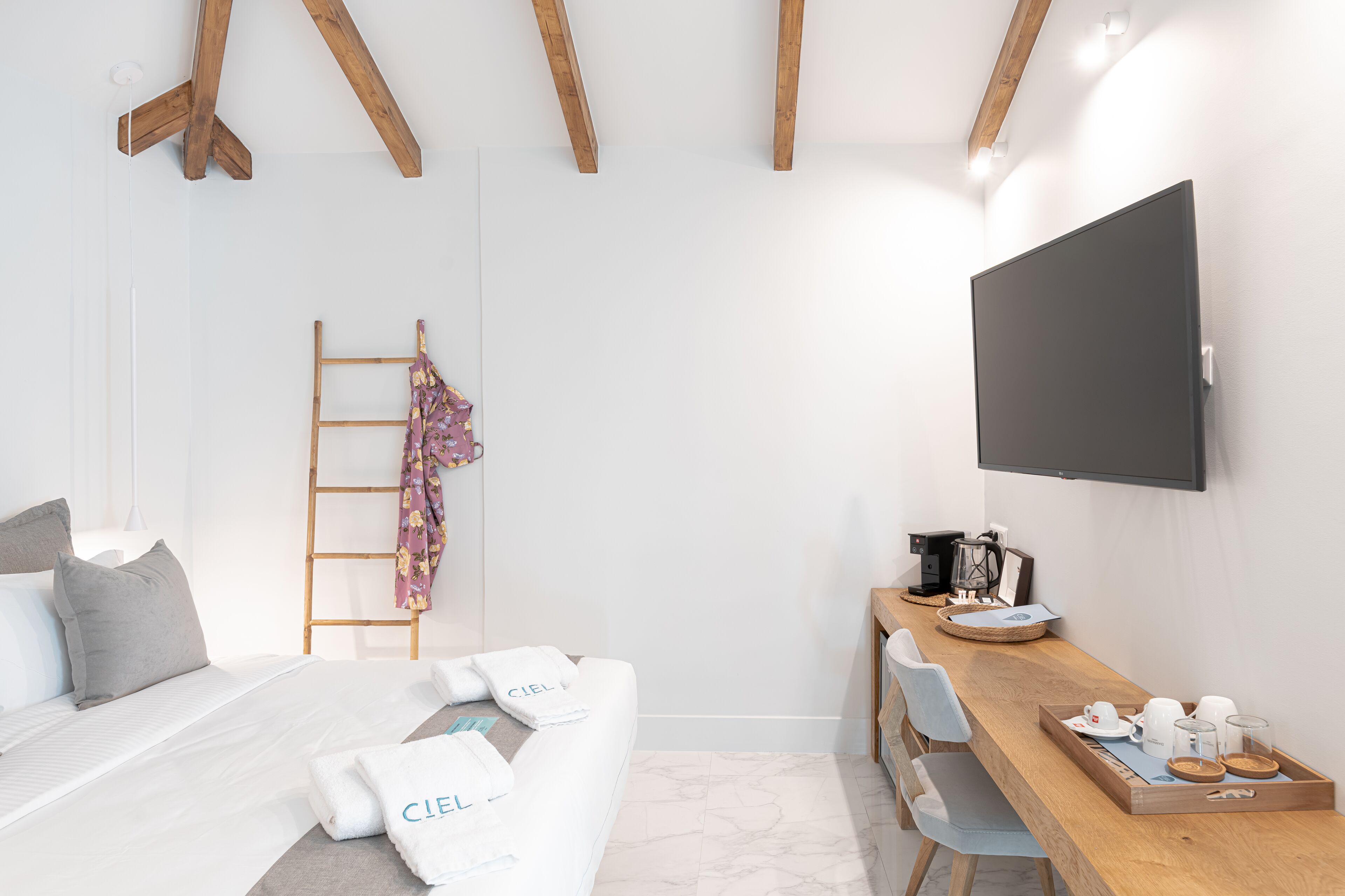 Ein modernes Hotelzimmer mit Bett, Schreibtisch mit Kaffeemaschine und Wandfernseher.