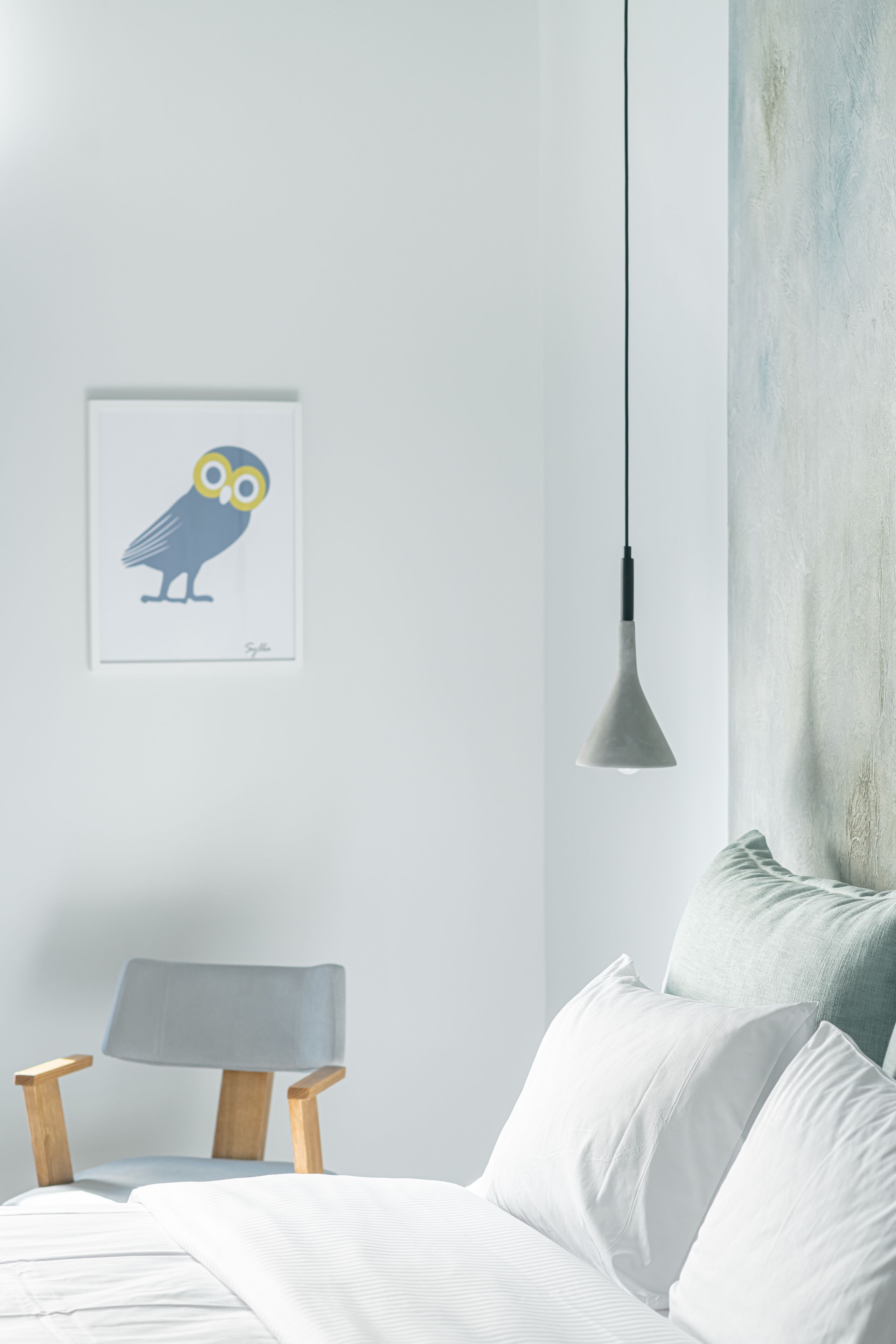 A bedroom with a bed, a chair, a hanging light, and a wall with a framed picture.