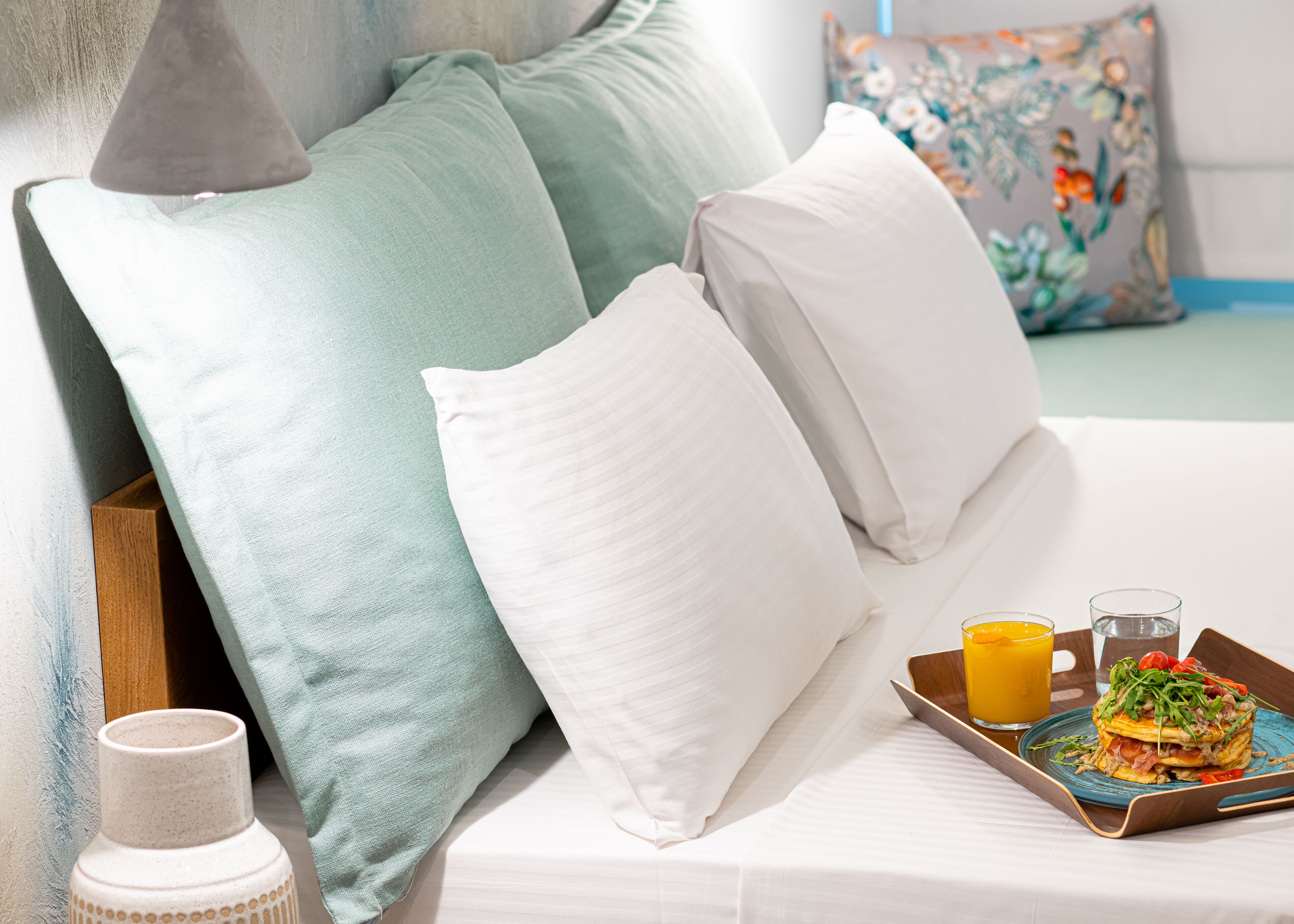 Una cama bien hecha con almohadas, una bandeja con desayuno y un florero.