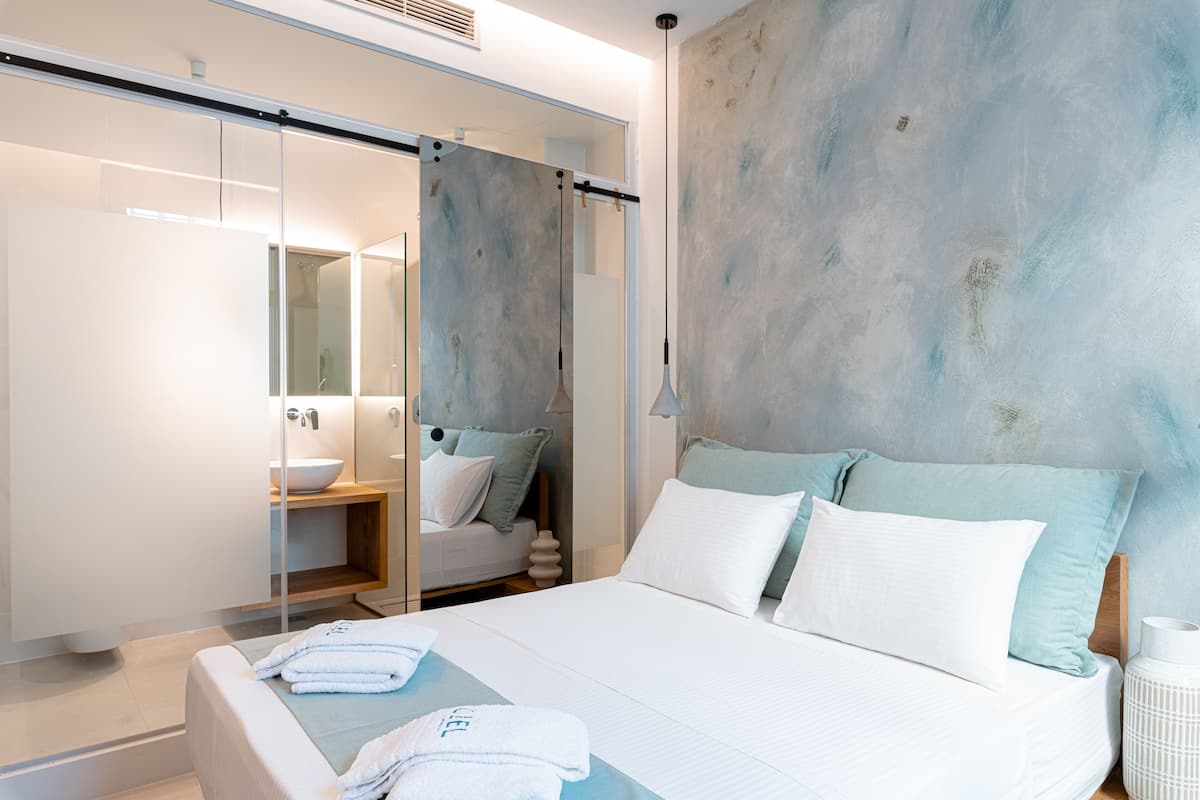 Quarto de hotel moderno com uma cama grande, chuveiro de vidro e vista para o banheiro.
