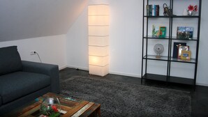 Un salon moderne avec un canapé gris, une table basse en bois sur laquelle repose un vase en verre, une bibliothèque noire et un grand lampadaire.