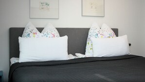 Un lit avec une tête de lit grise, des oreillers blancs ornés de motifs floraux et deux œuvres d’art encadrées accrochées au mur au-dessus.