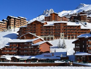A snow-covered mountain resort with multiple wooden buildings, including a restaurant and a ski lodge.