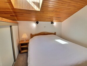 A bedroom with a wooden ceiling, a bed, a nightstand with a lamp, and a wall-mounted light fixture.