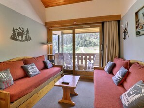 A cozy room with two sofas, a table, and a view of a forested area through a sliding door.