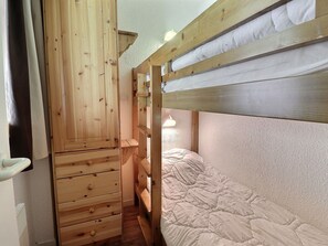 A bunk bed room with wooden walls, a small desk, and a bedside lamp.