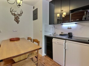 A compact kitchen with a wooden dining table, a built-in dishwasher, and a microwave above the counter.
