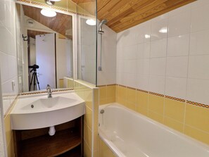 A bathroom with a white sink, a glass-enclosed shower, and yellow-tiled walls.