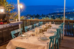An outdoor dining area with a view of a lake and cityscape at dusk. - Kamaya Suites (Emek HaYarden)