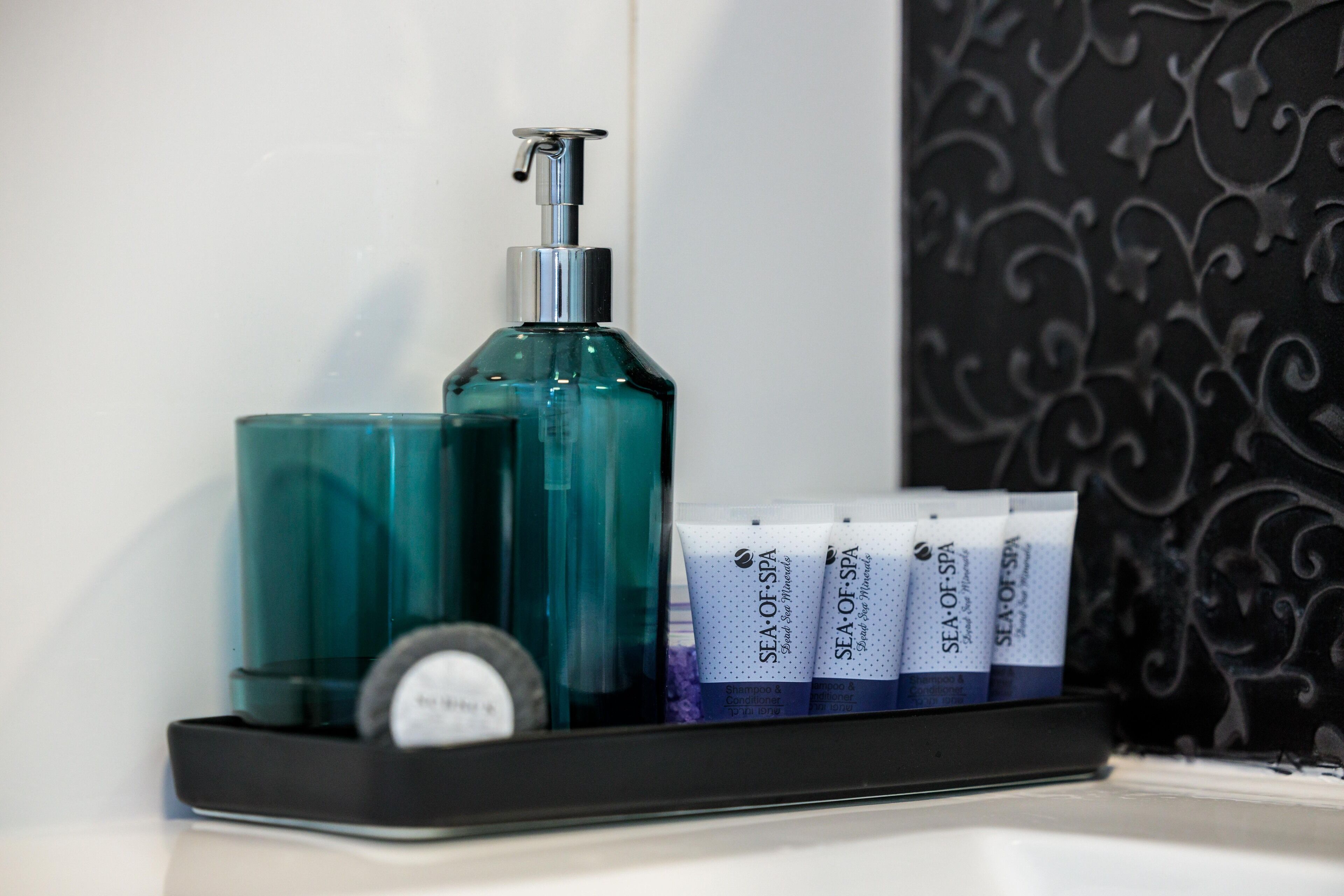 A bathroom shelf with a teal bottle, a pump dispenser, and several tubes of Sea of Spa products.