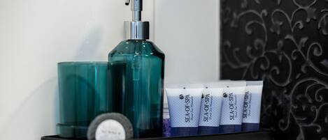A bathroom shelf with a teal bottle, a pump dispenser, and several tubes of Sea of Spa products.