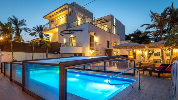 A modern two-story house with a swimming pool, outdoor seating, and palm trees. - Kamaya Suites (Emek HaYarden)