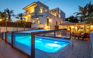 Une maison moderne à deux étages dotée d’une piscine, d’un espace salon extérieur et de palmiers.