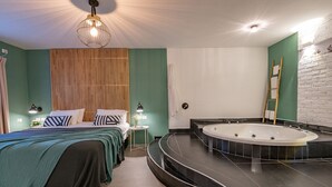A modern bedroom with a large bed, a separate sleeping area, a built-in bathtub, and a wooden slat wall. - Kamaya Suites (Emek HaYarden)
