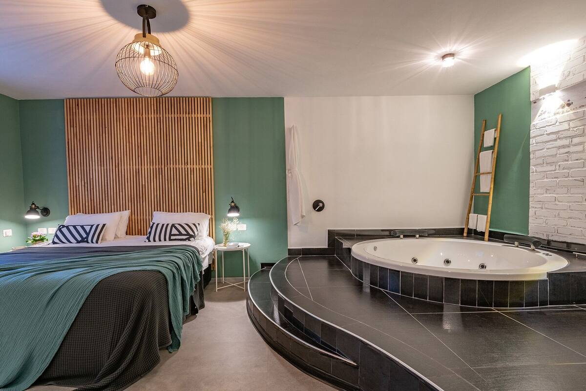 Een moderne slaapkamer met een groot bed, een afgescheiden slaapgedeelte, een inbouwbad en een wand van houten latten.