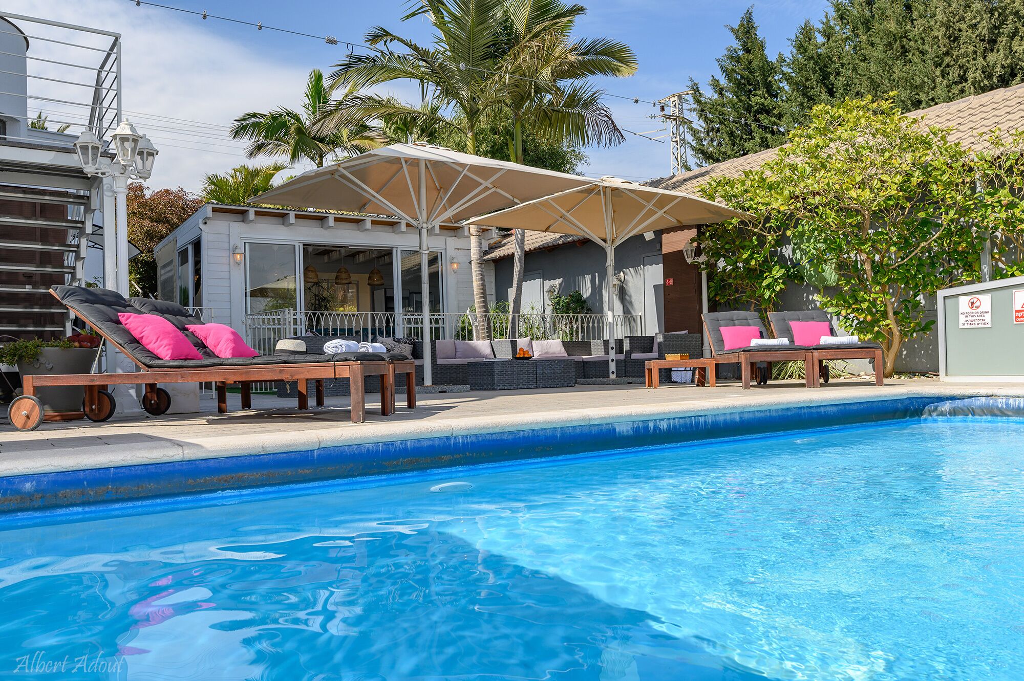 Un espace piscine avec des chaises longues, un coin salon abrité et une vue sur un immeuble d’habitation.