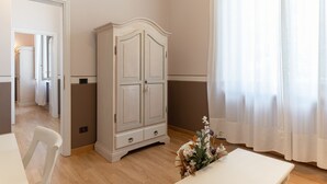 A room with a white cabinet, a table, and a chair. There is a door leading to another room. - Villa Romantica (Lucca)