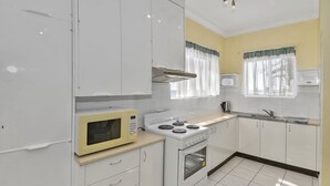A kitchen with white cabinets, a microwave, a stove, and a sink. - Beachside at The Entrance (The Entrance)