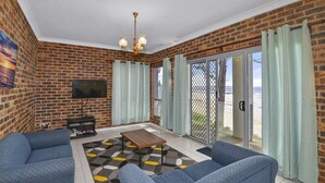 A living room with a brick wall, a flat-screen TV, a coffee table, and two sofas. - Beachside at The Entrance (The Entrance)