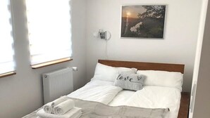 A single bed with a wooden frame, white bedding, and a pillow with "love" written on it. There is a radiator below the window, a small bedside table, and a rug on the floor. - Cozy Studio 2 Rosenburgblick near the Moselle (Zeltingen-Rachtig)