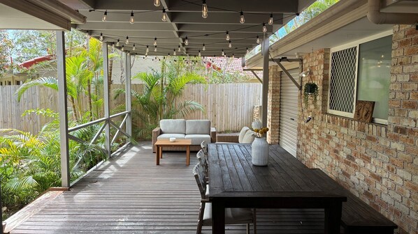 An outdoor patio with a wooden deck, a sofa, a table, and a brick wall.