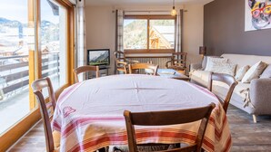 A cozy room with a dining table, chairs, a sofa, and a TV. - 3* Apartment, 2 bedrooms, 6 guests, near slopes, WIFI (La Clusaz)