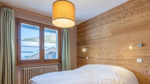 A bedroom with a bed, a window with curtains, a wooden wall, and a ceiling light fixture. - 3* Apartment, 2 bedrooms, 6 guests, near slopes, WIFI (La Clusaz)