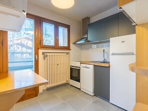 A kitchen with a built-in oven, a dishwasher, a refrigerator, and a window with a view of trees. - 3* Apartment, 2 bedrooms, 6 guests, near slopes, WIFI (La Clusaz)