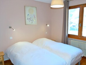Una habitación con dos camas, una ventana con vistas, una lámpara de pared y un radiador.