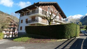 A multi-story building with balconies, a hedge in front, and a mountain backdrop. - 3* Apartment, 2 bedrooms, 6 guests, near slopes, WIFI (La Clusaz)